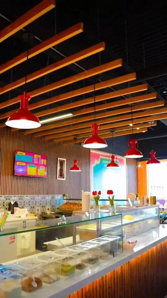 Chatori Gali at Mayfield: a wood-slat ceiling over red pendant lights and a long glass-front chaat counter