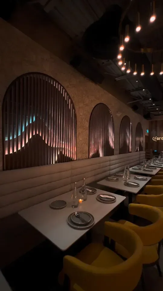 Desi Bar & Grill dining room: arched booths backlit against slat walls, with mustard chairs at set tables